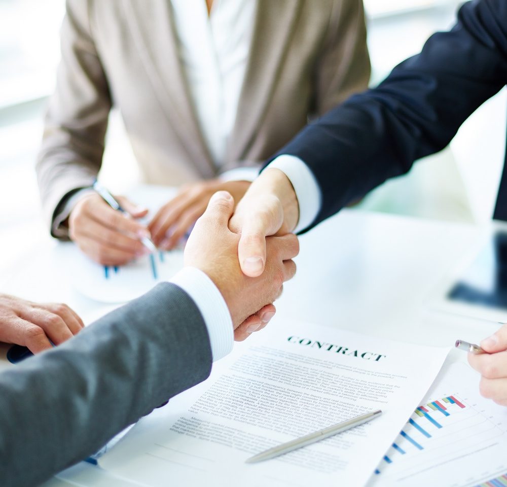 Image of business partners handshaking over business objects on workplace